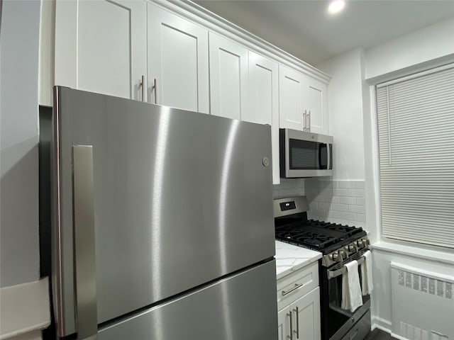 kitchen with appliances with stainless steel finishes, radiator, white cabinets, and backsplash