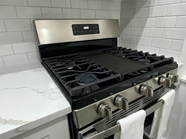 interior details with tasteful backsplash, gas stove, and white cabinets