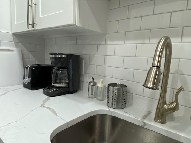 room details with light stone countertops, sink, decorative backsplash, and white cabinets