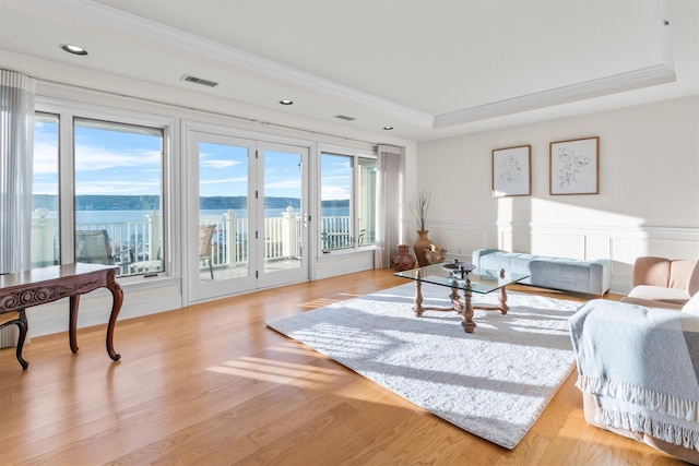 living room with a water view, ornamental molding, a raised ceiling, and light hardwood / wood-style flooring