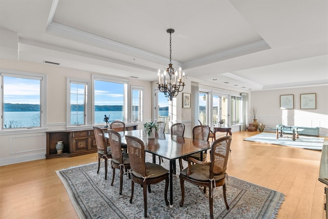 dining area with a water view, a healthy amount of sunlight, light hardwood / wood-style flooring, and a tray ceiling