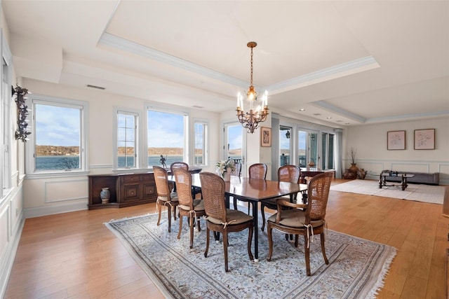 dining area featuring crown molding, a tray ceiling, light hardwood / wood-style floors, and a water view