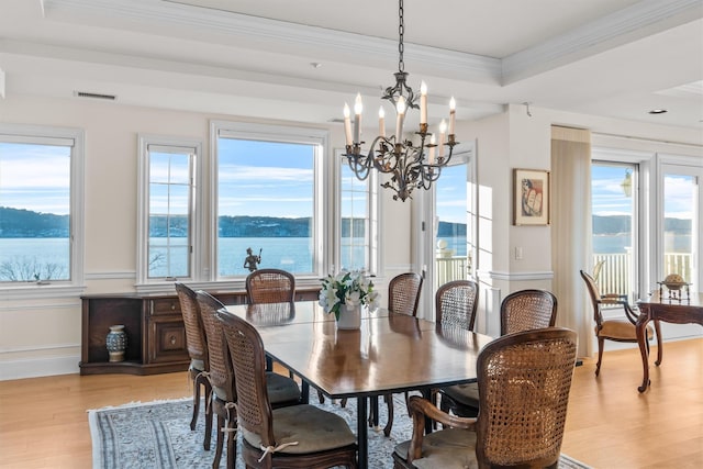 dining space featuring a chandelier, a tray ceiling, crown molding, a water view, and light wood-type flooring