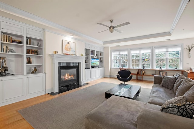 living room featuring ceiling fan, ornamental molding, a raised ceiling, and light wood-type flooring