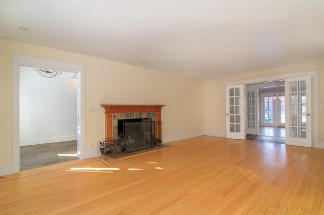 unfurnished living room featuring a tiled fireplace, hardwood / wood-style flooring, and french doors