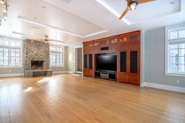 unfurnished living room with a tray ceiling, ceiling fan, and light wood-type flooring