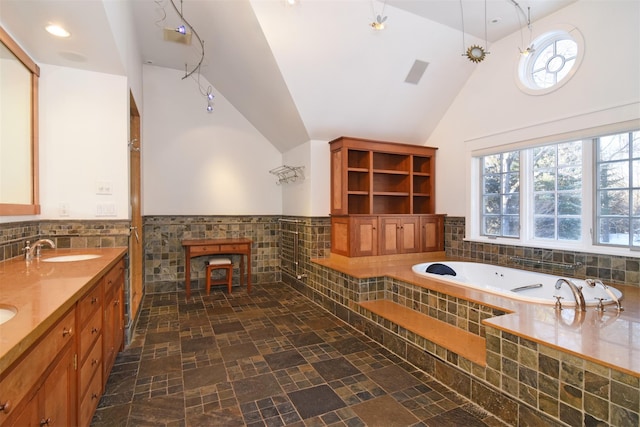 bathroom with a relaxing tiled tub, vanity, high vaulted ceiling, and tile walls