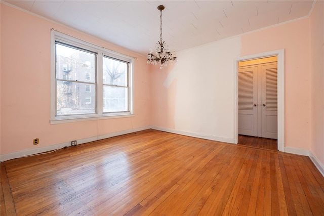 empty room with hardwood / wood-style floors, ornamental molding, and an inviting chandelier