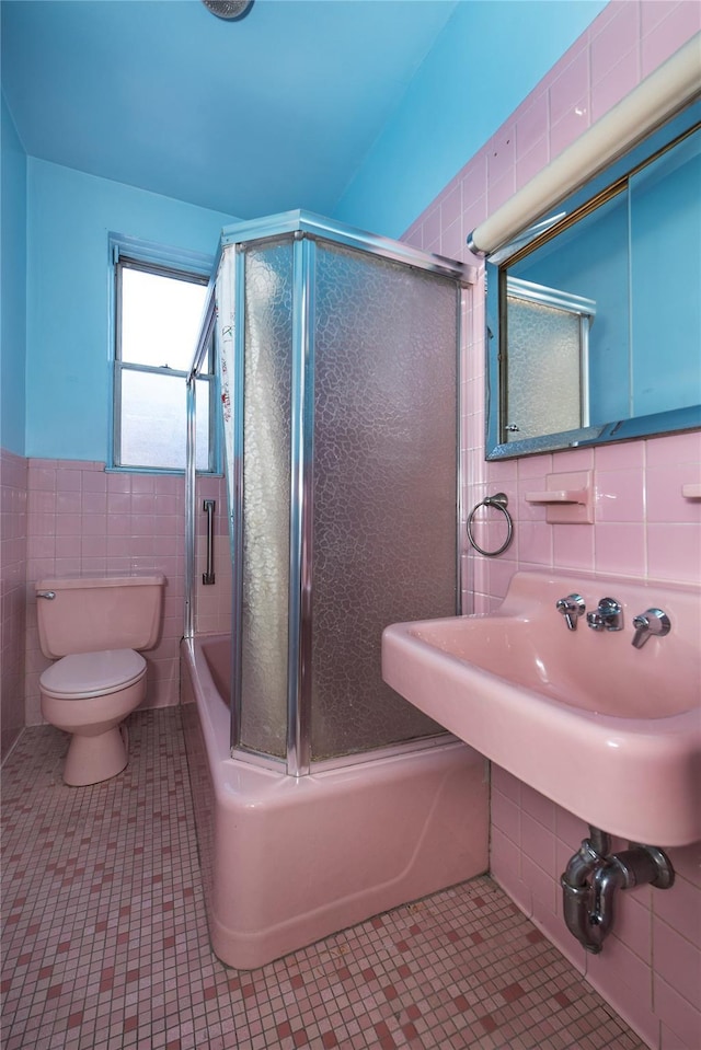 bathroom with toilet, bath / shower combo with glass door, tile walls, and tile patterned flooring