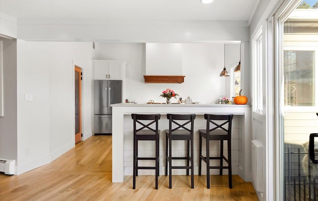 kitchen with high quality fridge, white cabinets, a breakfast bar area, and light wood-type flooring