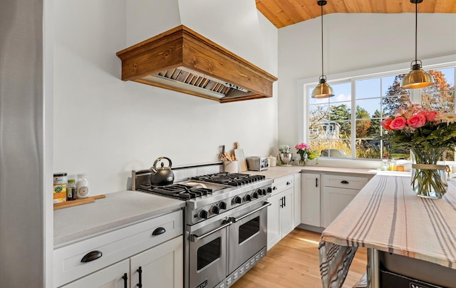 kitchen with premium range hood, white cabinets, decorative light fixtures, range with two ovens, and lofted ceiling