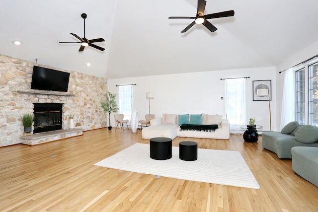 living room featuring high vaulted ceiling, a fireplace, light hardwood / wood-style floors, and ceiling fan