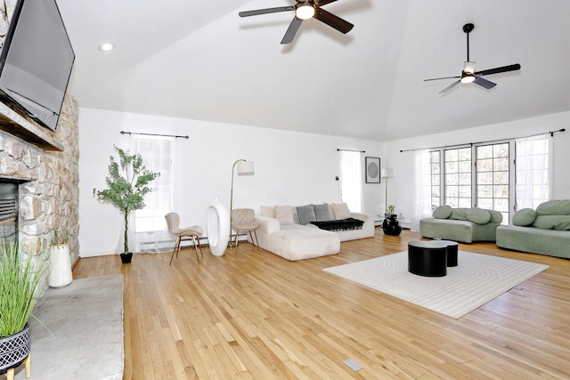 living room with high vaulted ceiling, light wood-type flooring, baseboard heating, ceiling fan, and a fireplace