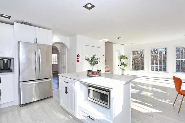 kitchen with white cabinetry, light stone counters, a kitchen island, and appliances with stainless steel finishes