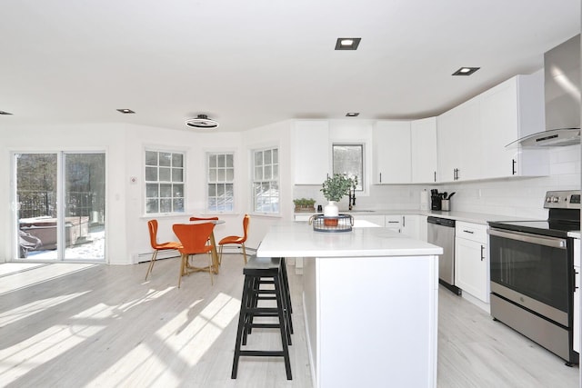 kitchen featuring stainless steel appliances, white cabinetry, a center island, and wall chimney range hood