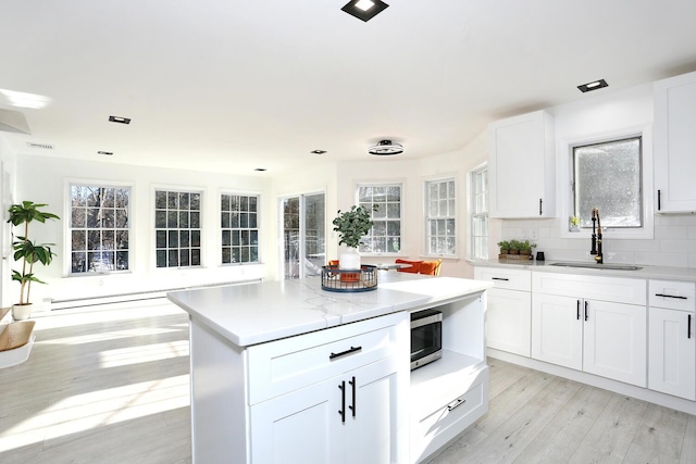 kitchen featuring sink, light hardwood / wood-style flooring, white cabinetry, backsplash, and a kitchen island