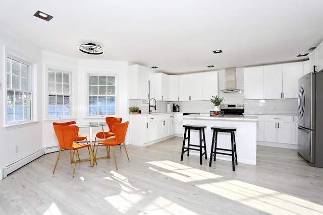 kitchen featuring a kitchen island, white cabinetry, backsplash, stainless steel appliances, and wall chimney range hood