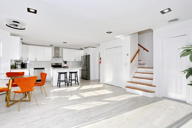 kitchen featuring wall chimney exhaust hood, white cabinetry, a kitchen breakfast bar, a kitchen island, and stainless steel appliances