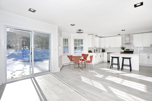 kitchen with a kitchen island, a breakfast bar, white cabinetry, decorative backsplash, and wall chimney range hood