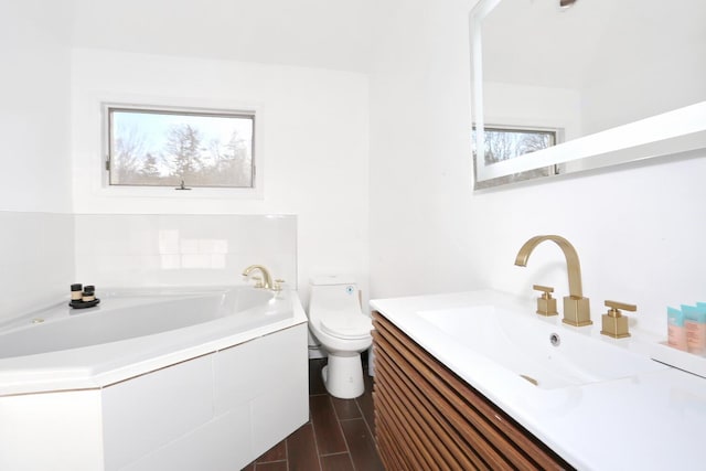 bathroom with vanity, tiled tub, and toilet