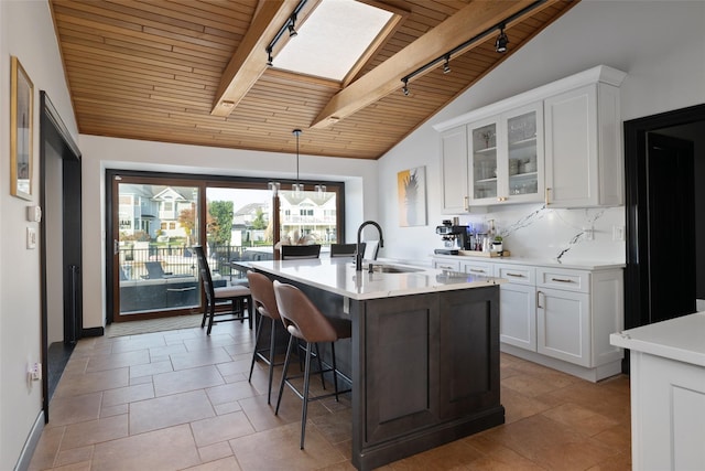 kitchen featuring wood ceiling, an island with sink, lofted ceiling with skylight, and white cabinets