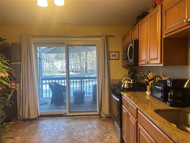 kitchen featuring gas range oven, stone countertops, stainless steel microwave, and brown cabinets