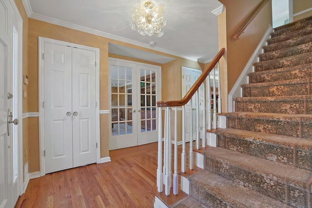 staircase with french doors, ornamental molding, an inviting chandelier, and hardwood / wood-style flooring