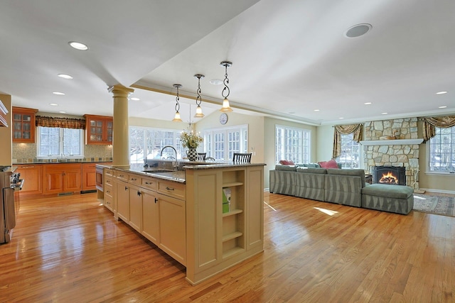 kitchen with sink, hanging light fixtures, light wood-type flooring, an island with sink, and light stone countertops