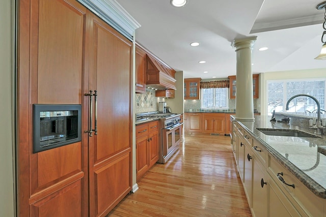 kitchen featuring sink, light wood-type flooring, dark stone counters, decorative columns, and range with two ovens