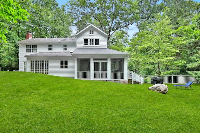 rear view of house featuring a sunroom and a lawn