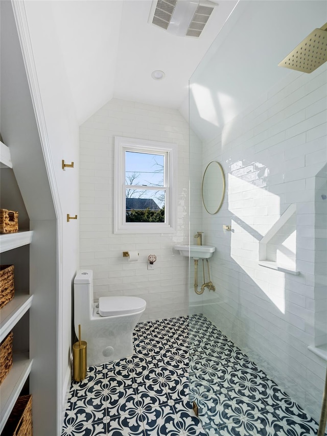 bathroom with toilet, a tile shower, lofted ceiling, and tile patterned flooring