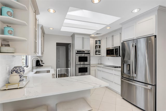 kitchen with sink, appliances with stainless steel finishes, white cabinetry, light stone countertops, and kitchen peninsula