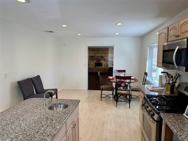 kitchen with light wood finished floors, appliances with stainless steel finishes, dark stone countertops, a sink, and recessed lighting