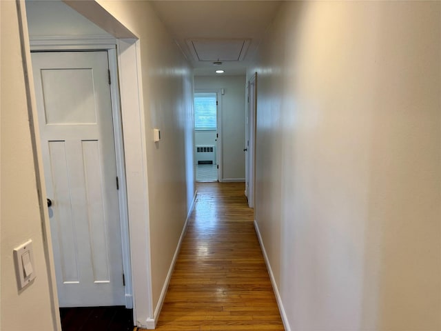 hallway with radiator, wood finished floors, attic access, and baseboards