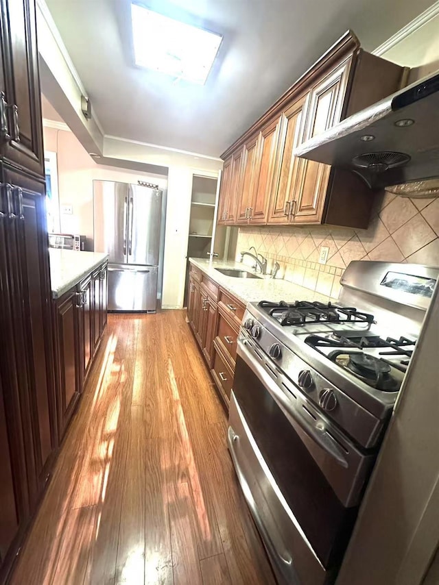 kitchen with hardwood / wood-style floors, a skylight, sink, stainless steel appliances, and wall chimney exhaust hood