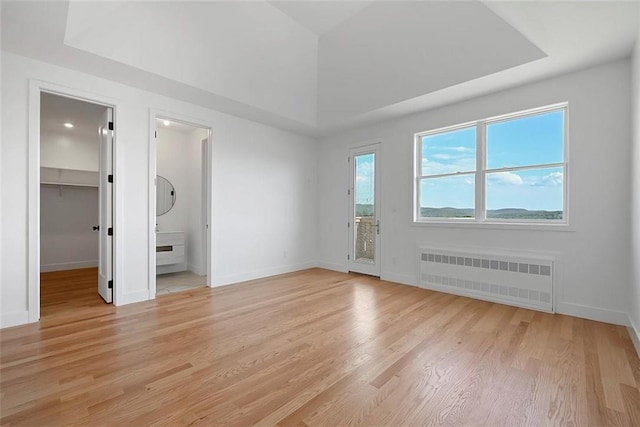 interior space featuring a spacious closet, radiator heating unit, ensuite bath, a closet, and light hardwood / wood-style flooring