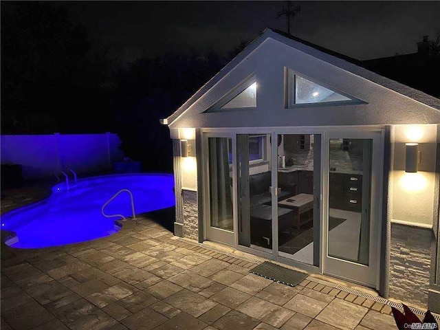 pool at night with pool water feature and a patio