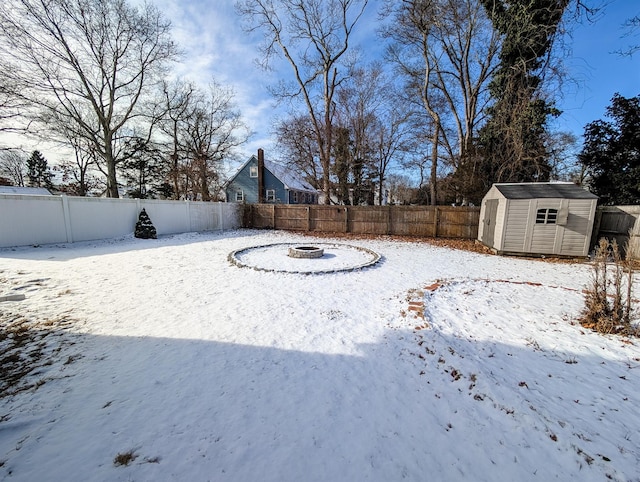 yard layered in snow with a fire pit and a storage unit