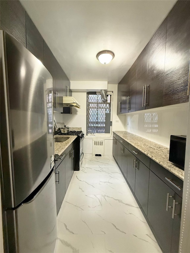 kitchen with light stone countertops, radiator heating unit, sink, stainless steel fridge, and black range with gas stovetop