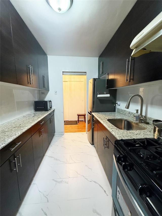 kitchen with black refrigerator, light stone countertops, decorative backsplash, gas range, and sink