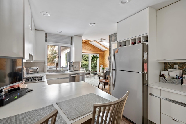 kitchen featuring kitchen peninsula, appliances with stainless steel finishes, sink, white cabinets, and lofted ceiling