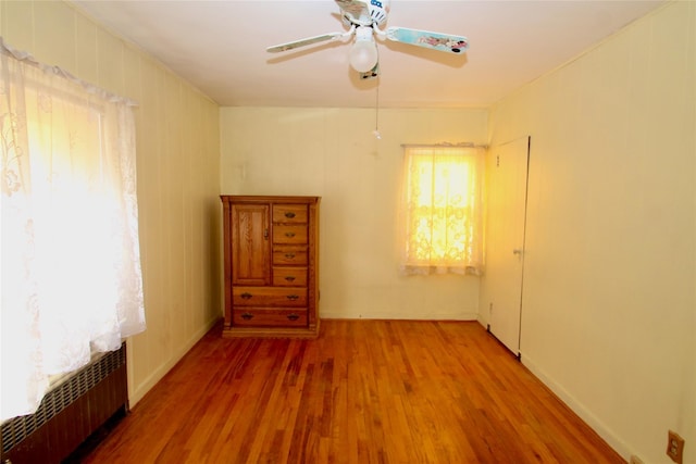 empty room with ceiling fan, radiator, and wood-type flooring