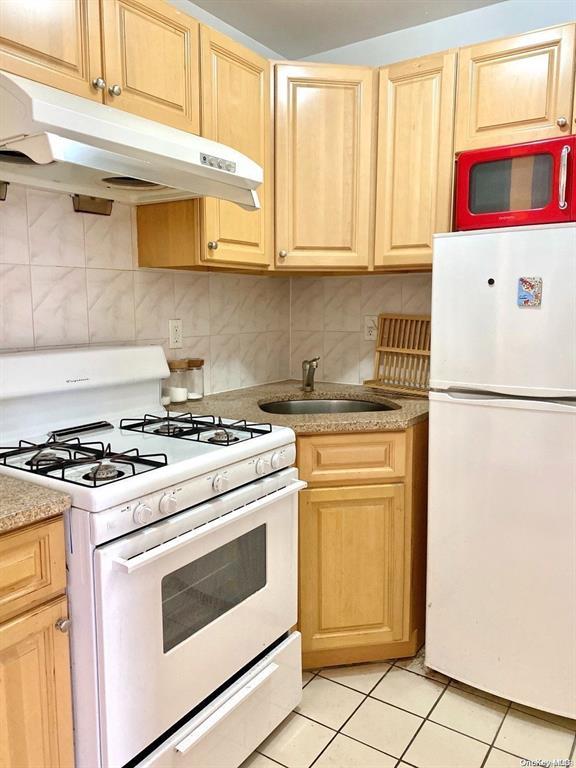 kitchen featuring white appliances, tasteful backsplash, light tile patterned floors, sink, and light brown cabinets