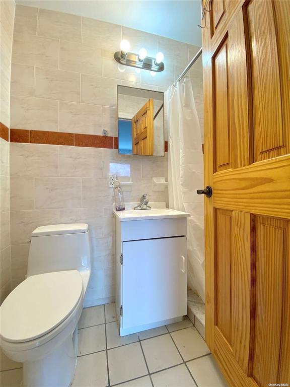 bathroom with tile patterned flooring, vanity, tile walls, toilet, and walk in shower