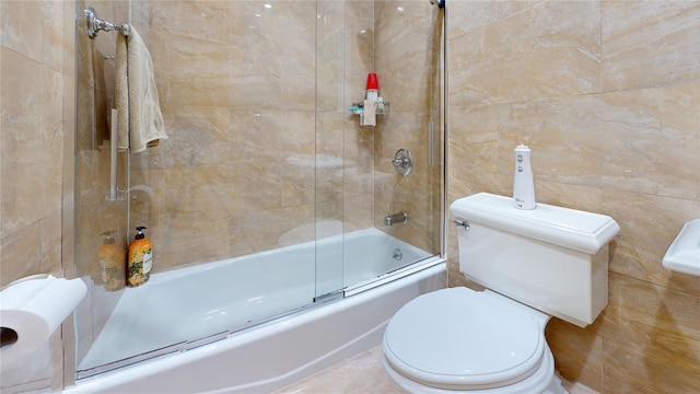 bathroom featuring toilet, shower / bath combination with glass door, and tile walls