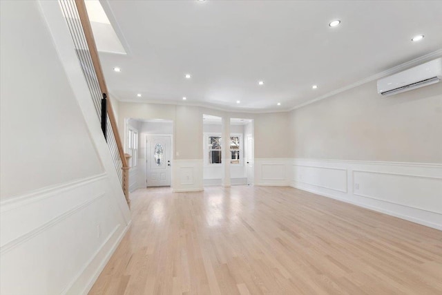 unfurnished living room featuring light hardwood / wood-style flooring, ornamental molding, and a wall mounted air conditioner