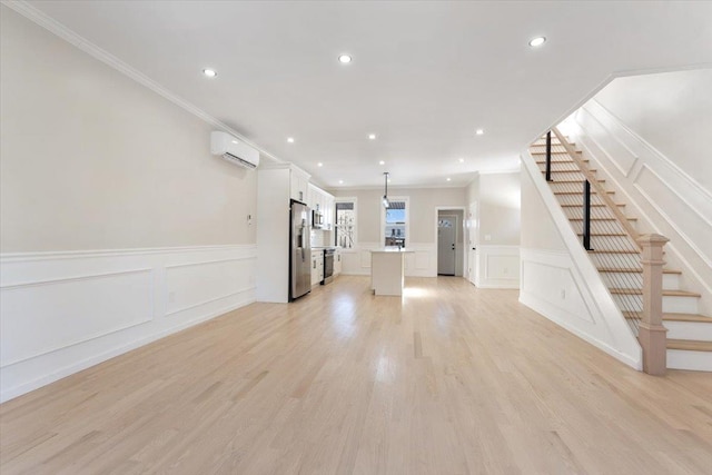 unfurnished living room with light wood-type flooring, ornamental molding, and a wall mounted air conditioner