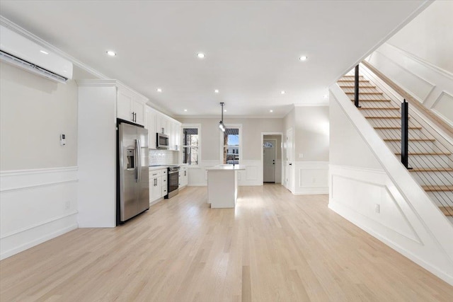 kitchen with crown molding, white cabinets, light wood-type flooring, decorative light fixtures, and stainless steel appliances