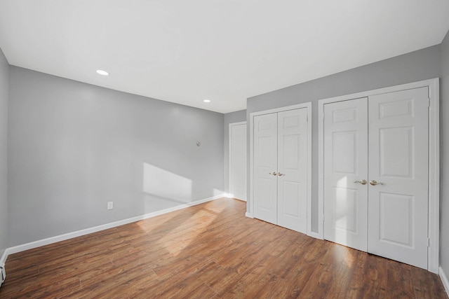 unfurnished bedroom featuring wood-type flooring and two closets