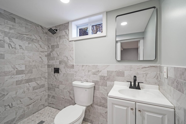 bathroom with a tile shower, toilet, tile walls, and vanity